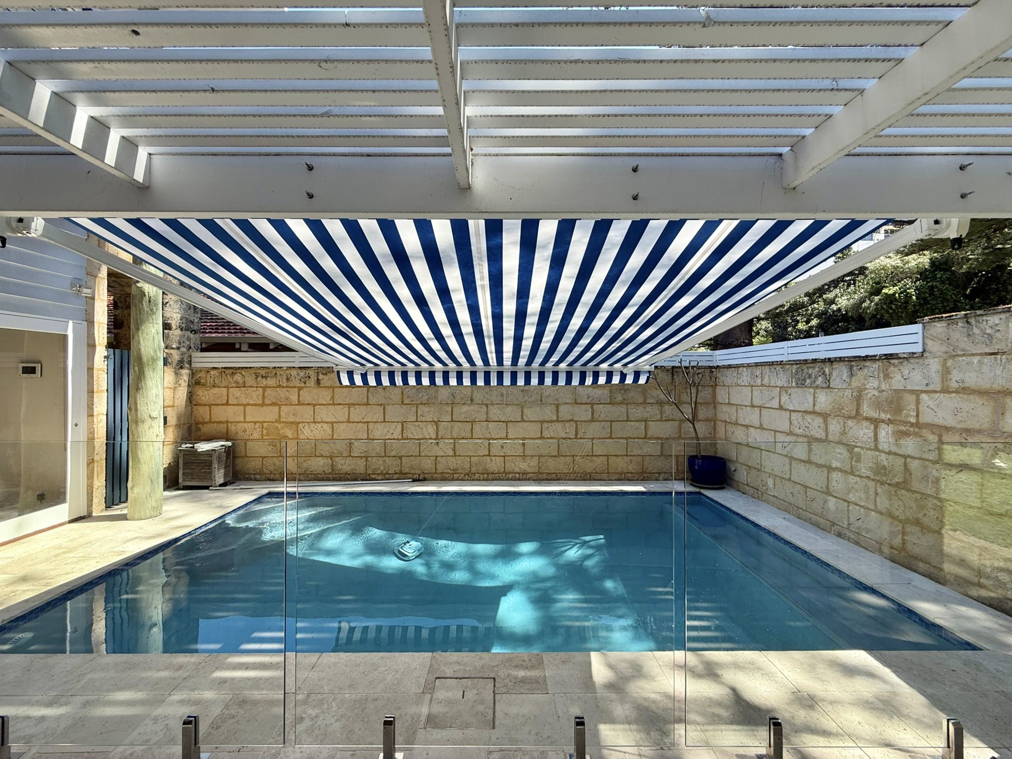 Retractable folding arm awning with blue and white striped fabric shading a pool area