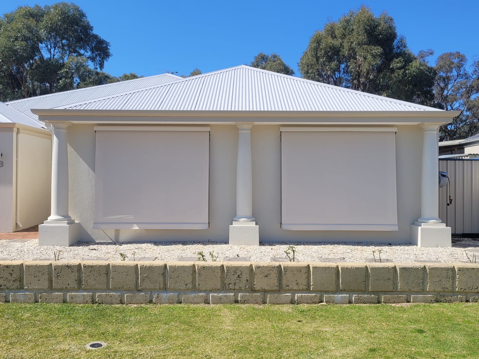 Cream outdoor blinds lowered over two windows on a modern rendered Perth home with classical columns