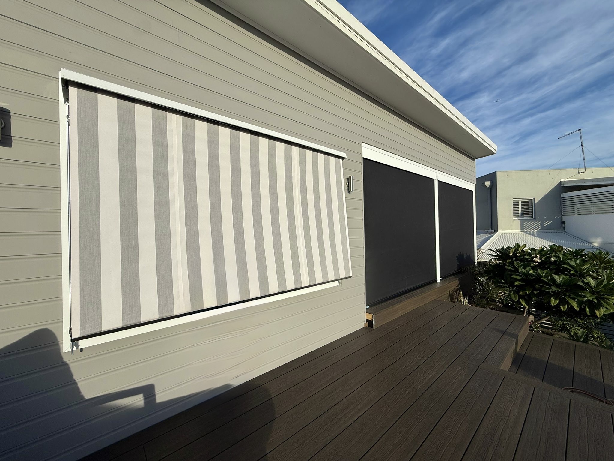 Grey striped fabric outdoor blind beside dark mesh blinds on a Perth home's timber deck