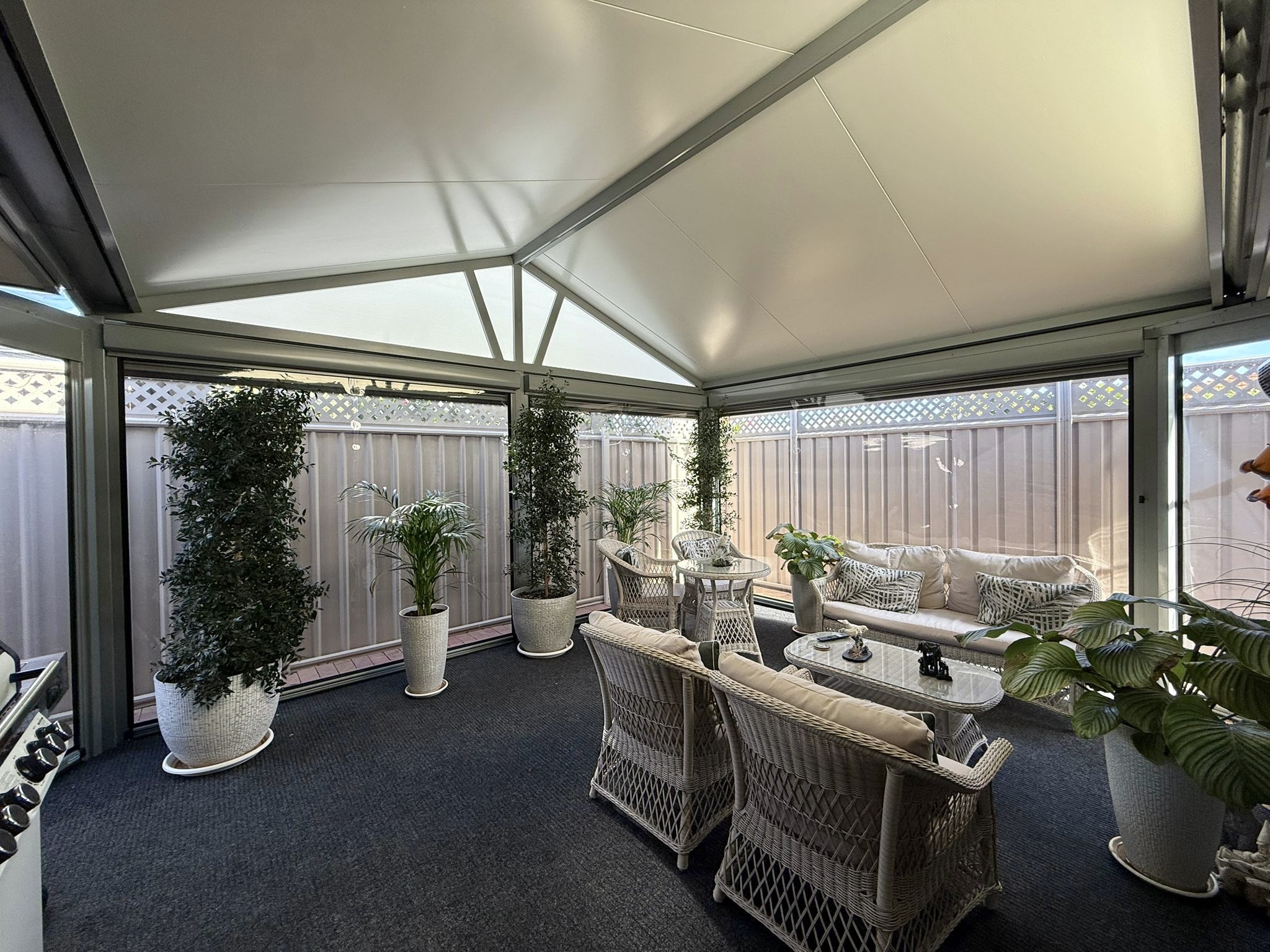Interior view of a Perth alfresco with mesh outdoor blinds allowing natural light through, white gabled roof and potted plants
