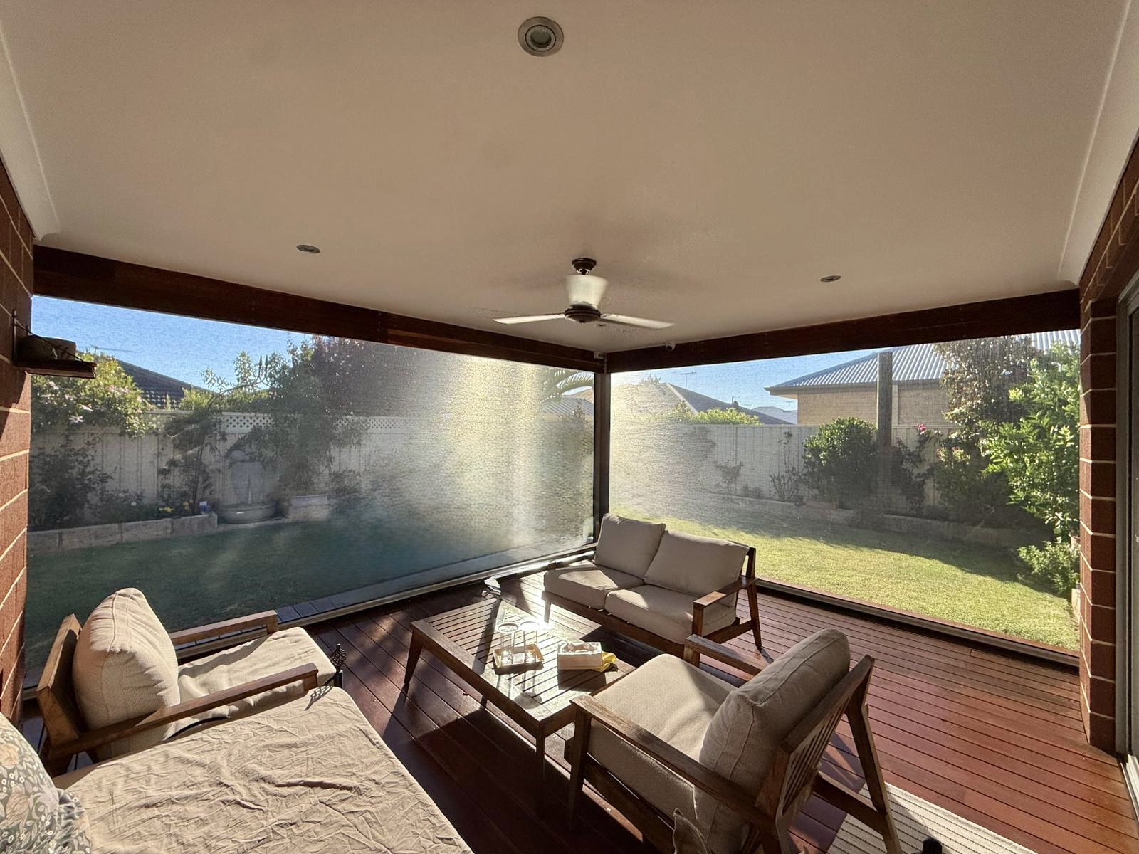 Clear PVC outdoor blinds lowered on a covered timber deck alfresco in Perth, with garden views and outdoor lounge furniture