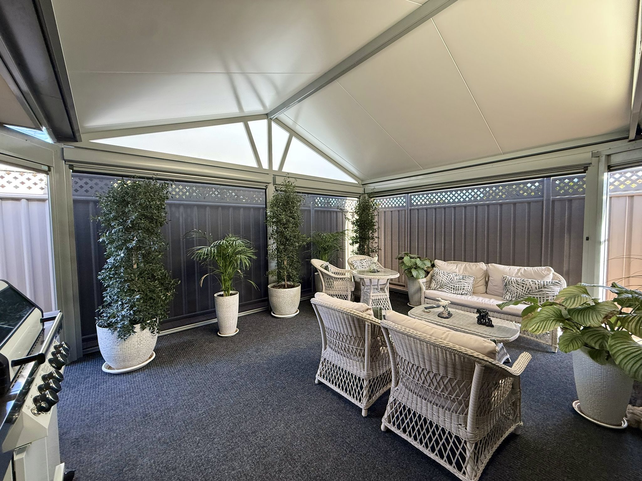 Interior view of a Perth outdoor room fully enclosed with light mesh outdoor blinds, white gabled roof structure and wicker furniture
