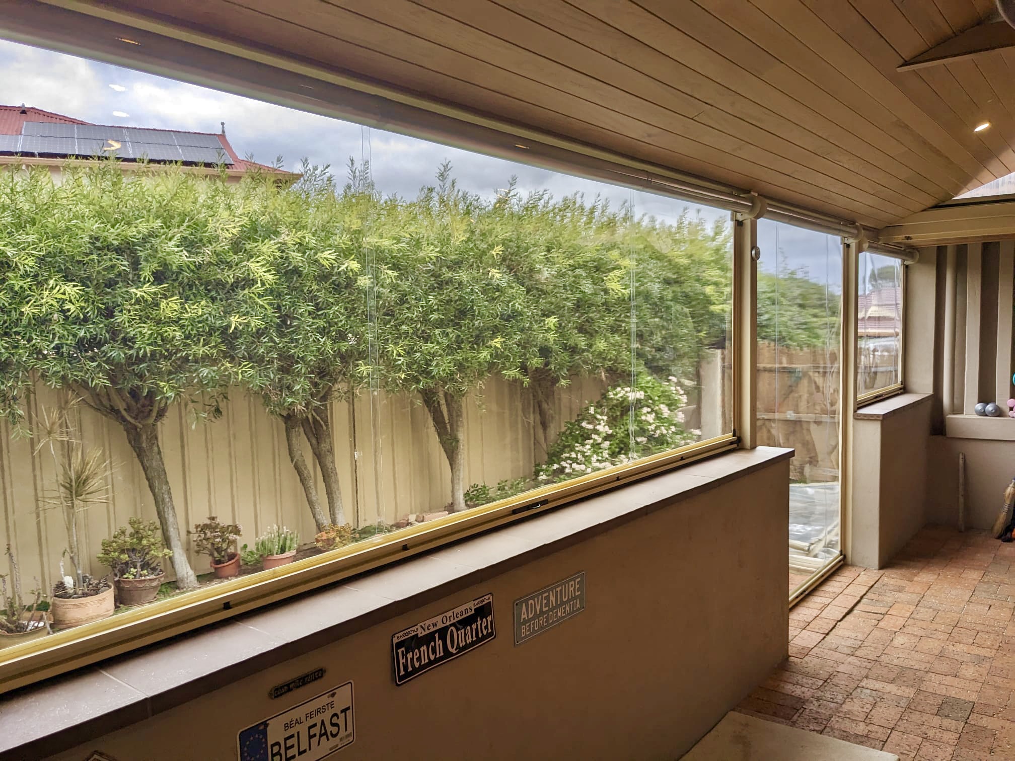 Interior view of a Perth verandah fully enclosed with clear PVC outdoor blinds, with an unobstructed view of the garden and surrounding trees